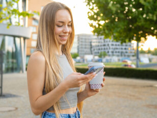 blonde hair woman smiles phone screen texting message standing street sunset scaled