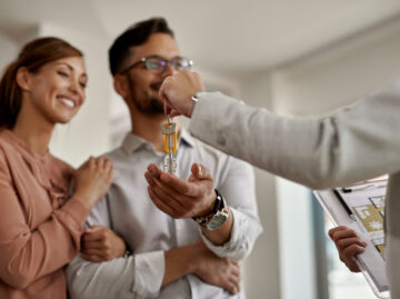 closeup real estate agent giving couple keys their new home scaled