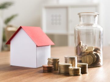 miniaturbank mit munzstapeln und glas daneben scaled