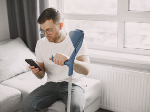 young man with broken leg home using smartphone scaled