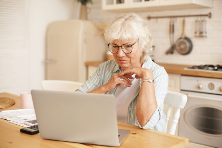 modern technology old people retirement gray haired female pensioner glasses filling loan application form online sitting front laptop reading information with serious focused look scaled